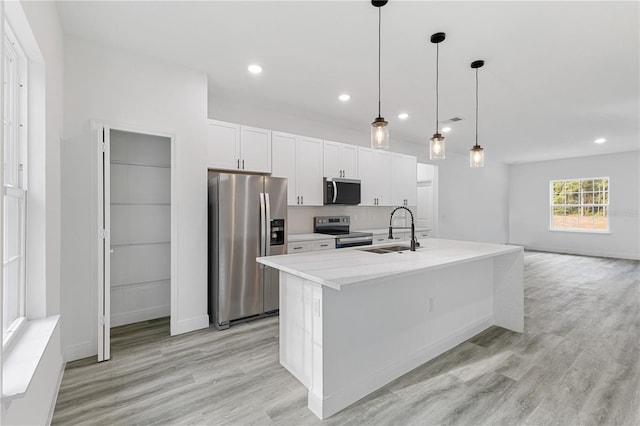 kitchen with sink, appliances with stainless steel finishes, a kitchen island with sink, white cabinets, and light wood-type flooring