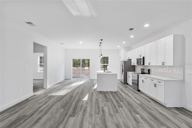 kitchen with white cabinetry, stainless steel appliances, pendant lighting, light hardwood / wood-style floors, and a kitchen island