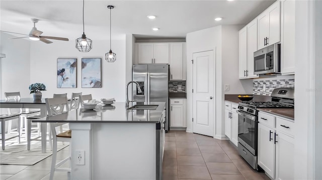 kitchen featuring decorative light fixtures, a center island with sink, tasteful backsplash, white cabinetry, and appliances with stainless steel finishes