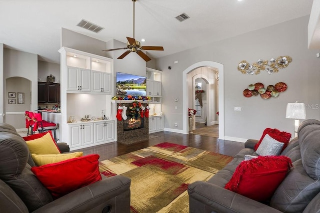 living room with arched walkways, dark wood-style flooring, visible vents, and a ceiling fan