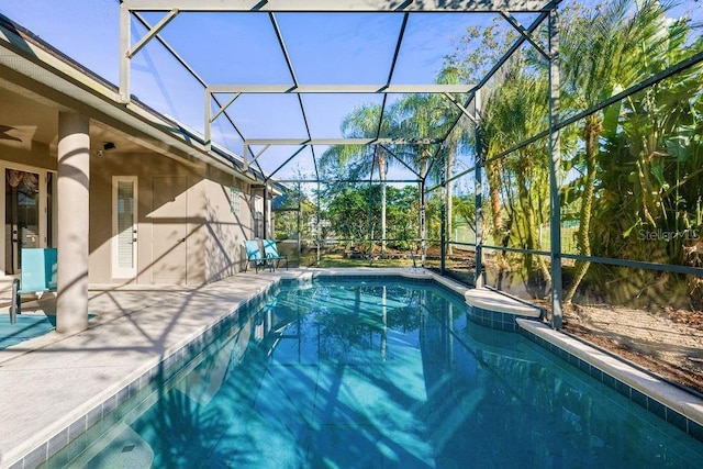 outdoor pool with glass enclosure, a ceiling fan, and a patio