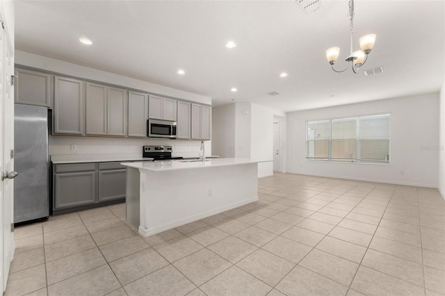 kitchen featuring gray cabinets, an island with sink, appliances with stainless steel finishes, decorative light fixtures, and a chandelier