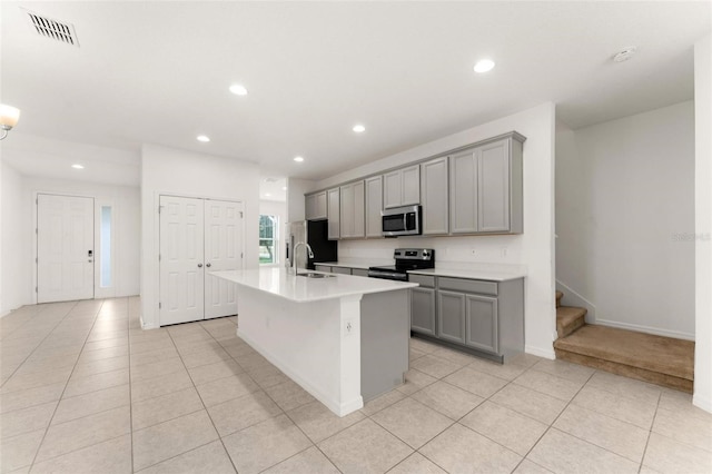 kitchen with gray cabinetry, sink, an island with sink, light tile patterned floors, and appliances with stainless steel finishes