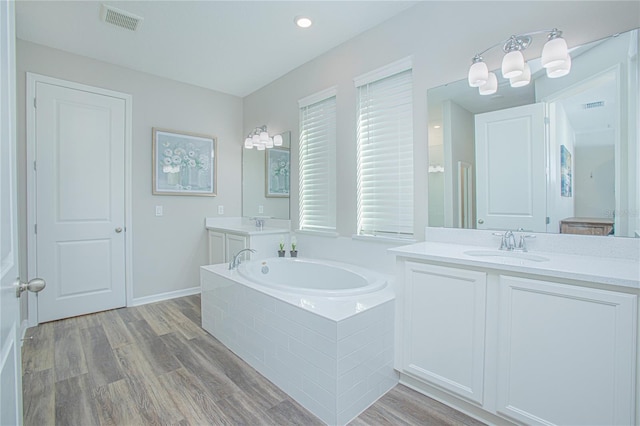 bathroom featuring hardwood / wood-style flooring, vanity, and a relaxing tiled tub