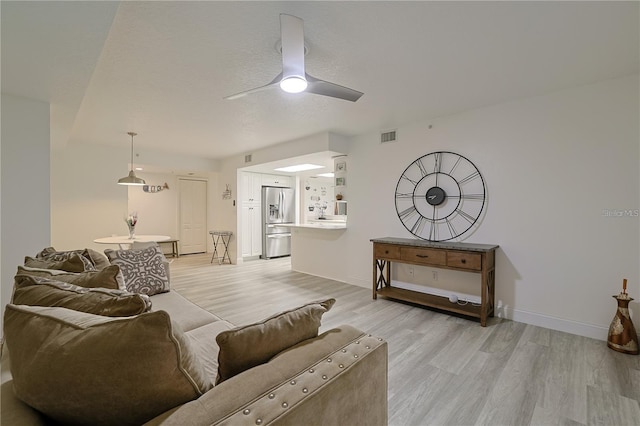 living room with ceiling fan, light hardwood / wood-style floors, and a textured ceiling