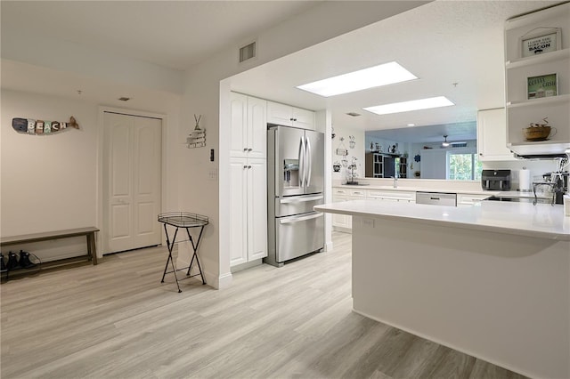 kitchen featuring a skylight, light hardwood / wood-style flooring, stainless steel fridge, kitchen peninsula, and white cabinets