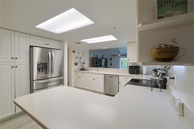 kitchen featuring appliances with stainless steel finishes, a skylight, white cabinets, kitchen peninsula, and light hardwood / wood-style flooring