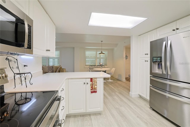 kitchen with hanging light fixtures, stainless steel appliances, light hardwood / wood-style floors, white cabinets, and kitchen peninsula