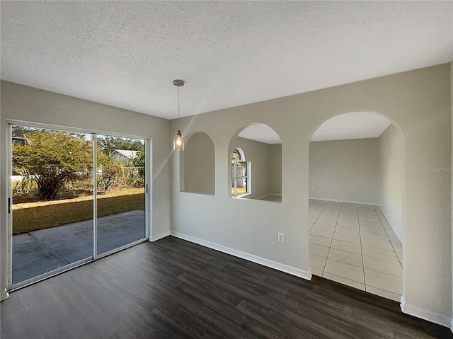 unfurnished room with a textured ceiling, a wealth of natural light, and dark wood-type flooring