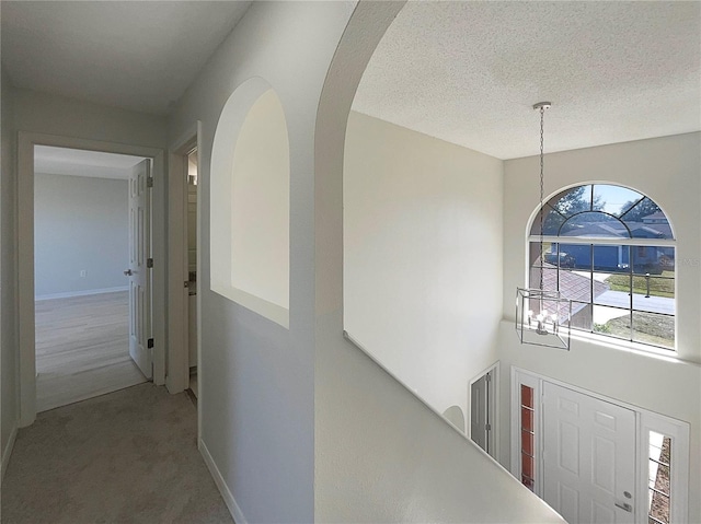 corridor featuring carpet, a chandelier, and a textured ceiling