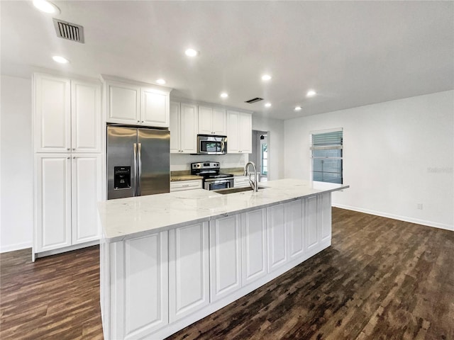 kitchen featuring light stone counters, stainless steel appliances, dark wood-type flooring, a large island with sink, and white cabinets