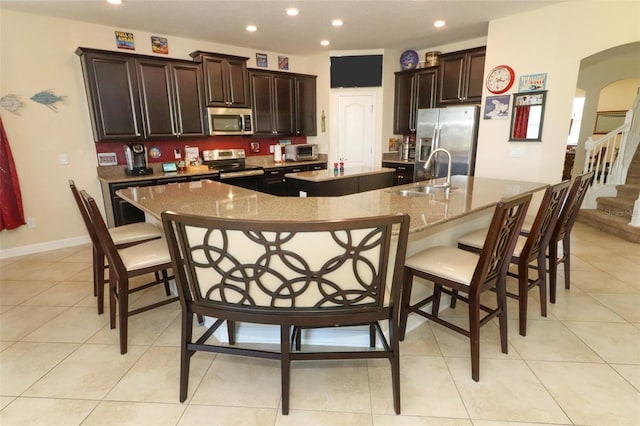 kitchen with a large island, sink, a breakfast bar area, light tile patterned flooring, and appliances with stainless steel finishes