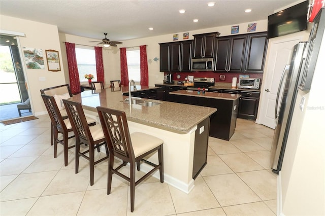 kitchen featuring a kitchen breakfast bar, sink, ceiling fan, an island with sink, and stainless steel appliances