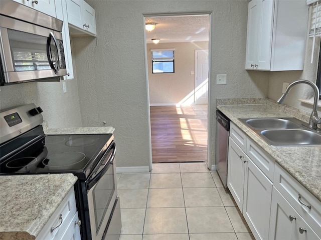 kitchen featuring sink, light wood-type flooring, a textured ceiling, appliances with stainless steel finishes, and white cabinetry