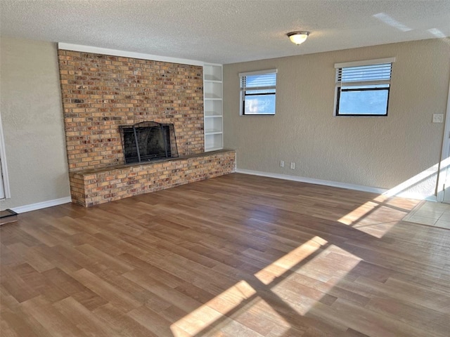 unfurnished living room featuring a fireplace, built in shelves, a textured ceiling, and hardwood / wood-style floors