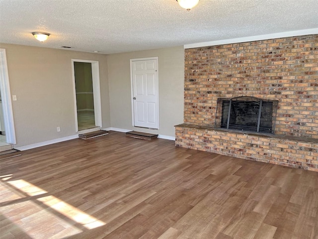 unfurnished living room with a textured ceiling, hardwood / wood-style flooring, and a brick fireplace