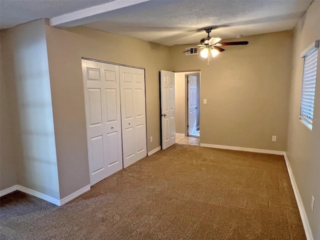 unfurnished bedroom featuring carpet, a textured ceiling, a closet, and ceiling fan