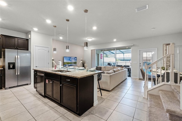 kitchen featuring sink, dishwashing machine, stainless steel fridge, hanging light fixtures, and a center island with sink