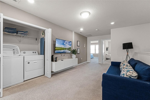 living room featuring washer and clothes dryer, light carpet, and a textured ceiling