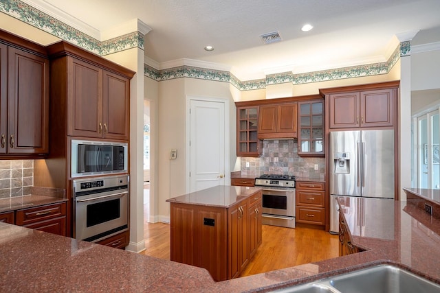 kitchen with a center island, stainless steel appliances, tasteful backsplash, ornamental molding, and light wood-type flooring