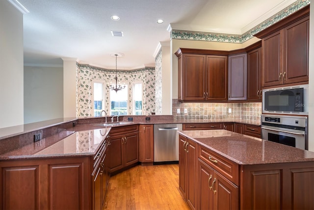 kitchen featuring kitchen peninsula, appliances with stainless steel finishes, ornamental molding, sink, and a chandelier