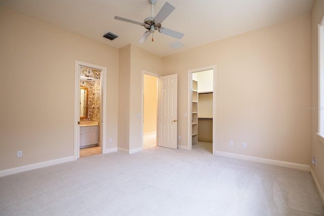 unfurnished bedroom with ensuite bathroom, ceiling fan, a walk in closet, and light carpet