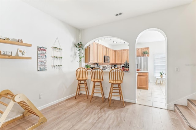 kitchen featuring appliances with stainless steel finishes, rail lighting, light hardwood / wood-style floors, and a breakfast bar area