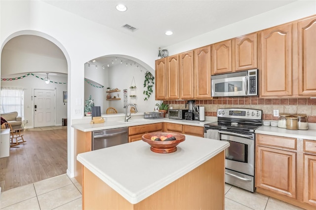 kitchen with sink, light hardwood / wood-style flooring, decorative backsplash, a kitchen island, and stainless steel appliances