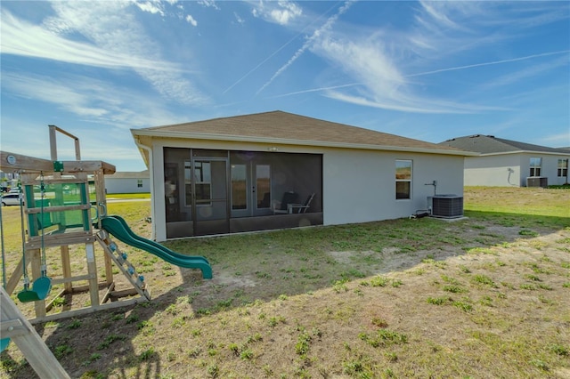 back of property with a sunroom, a playground, a lawn, and central AC