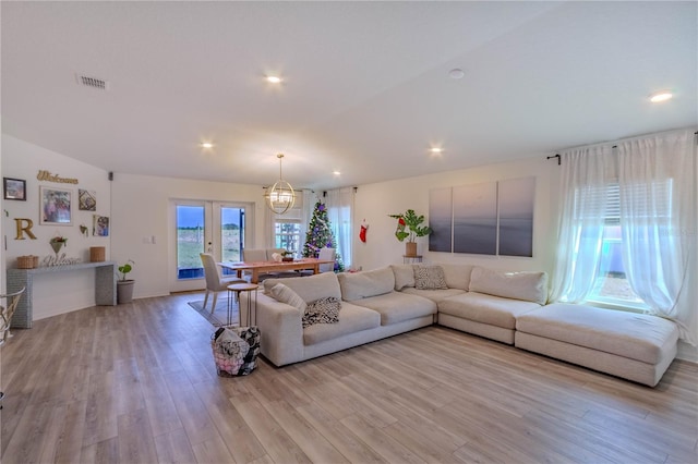 living room with light hardwood / wood-style flooring, a chandelier, and vaulted ceiling