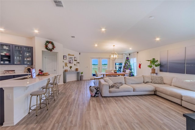 living room featuring vaulted ceiling, sink, a notable chandelier, and light hardwood / wood-style flooring