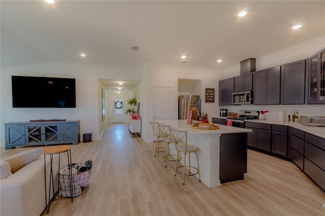 kitchen featuring appliances with stainless steel finishes, light wood-type flooring, a breakfast bar, dark brown cabinetry, and a kitchen island with sink