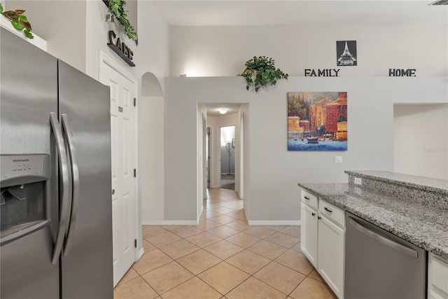 kitchen with white cabinets, light tile patterned floors, stainless steel appliances, and light stone countertops