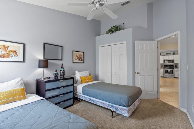 bedroom featuring a towering ceiling, a closet, light colored carpet, and ceiling fan