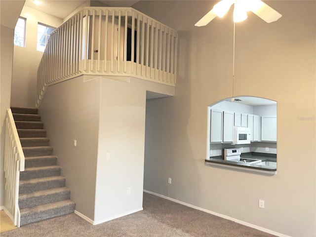 staircase featuring carpet, a towering ceiling, and ceiling fan