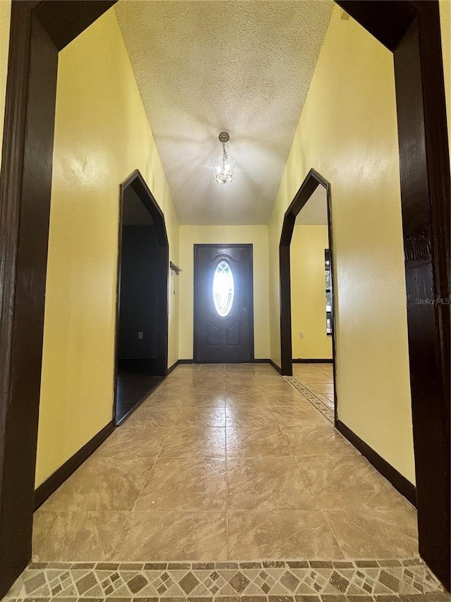 entryway with lofted ceiling, a textured ceiling, and a chandelier