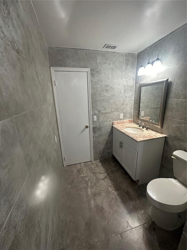 bathroom featuring vanity, toilet, and tile walls