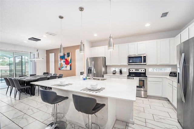 kitchen featuring pendant lighting, a center island with sink, sink, appliances with stainless steel finishes, and white cabinetry