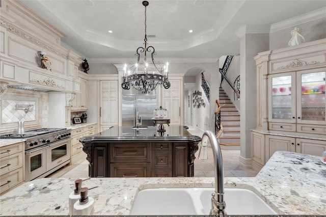 kitchen with high end appliances, sink, cream cabinetry, decorative light fixtures, and light stone counters