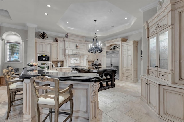 kitchen with stainless steel appliances, a large island with sink, dark stone countertops, cream cabinets, and pendant lighting