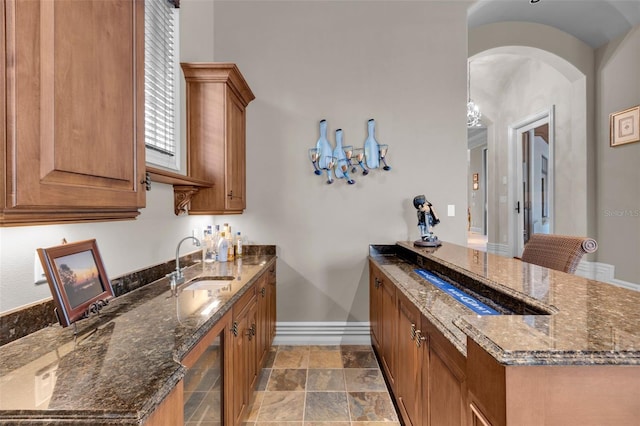 bar featuring sink, beverage cooler, and dark stone counters