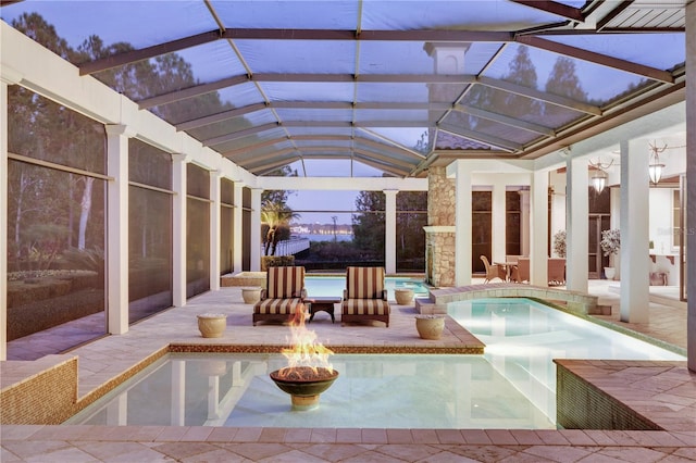 pool at dusk featuring glass enclosure, a patio, and a jacuzzi