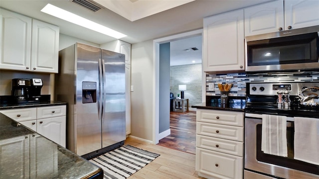 kitchen featuring stainless steel appliances, white cabinetry, dark stone counters, and light hardwood / wood-style flooring