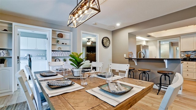 dining area featuring ceiling fan with notable chandelier, washing machine and dryer, and light hardwood / wood-style flooring