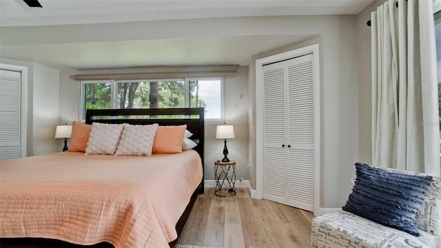 bedroom with ceiling fan, light hardwood / wood-style floors, and multiple closets