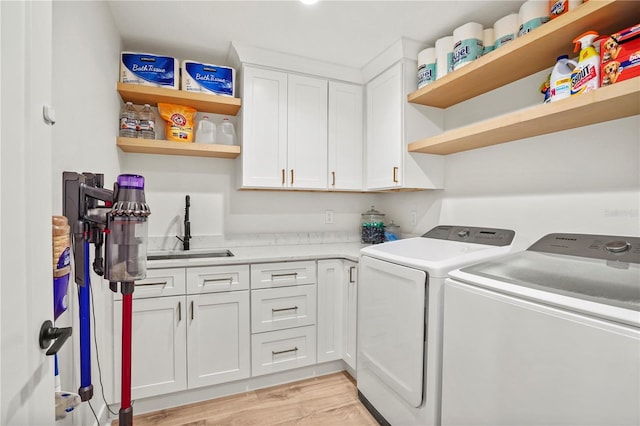 clothes washing area with cabinets, washer and clothes dryer, light hardwood / wood-style flooring, and sink