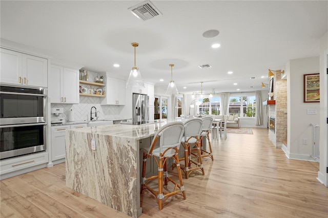 kitchen with white cabinetry, an island with sink, appliances with stainless steel finishes, hanging light fixtures, and light stone countertops