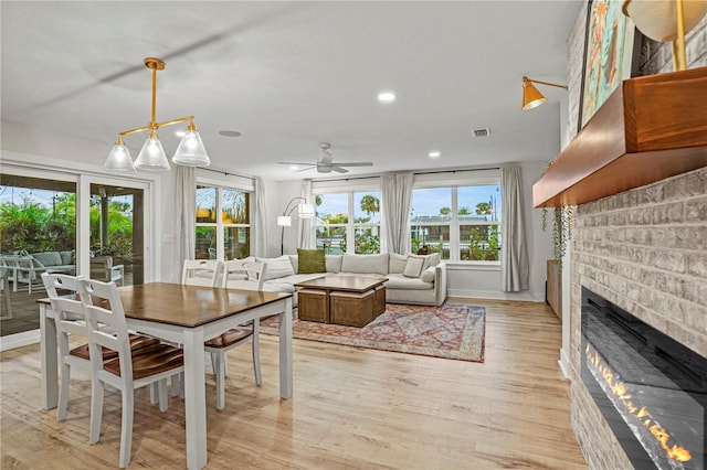 dining room with a brick fireplace, ceiling fan with notable chandelier, and light hardwood / wood-style flooring