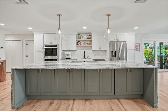 kitchen featuring hanging light fixtures, stainless steel appliances, white cabinets, and light stone counters