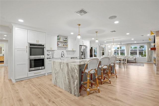 kitchen featuring decorative light fixtures, white cabinets, appliances with stainless steel finishes, and an island with sink